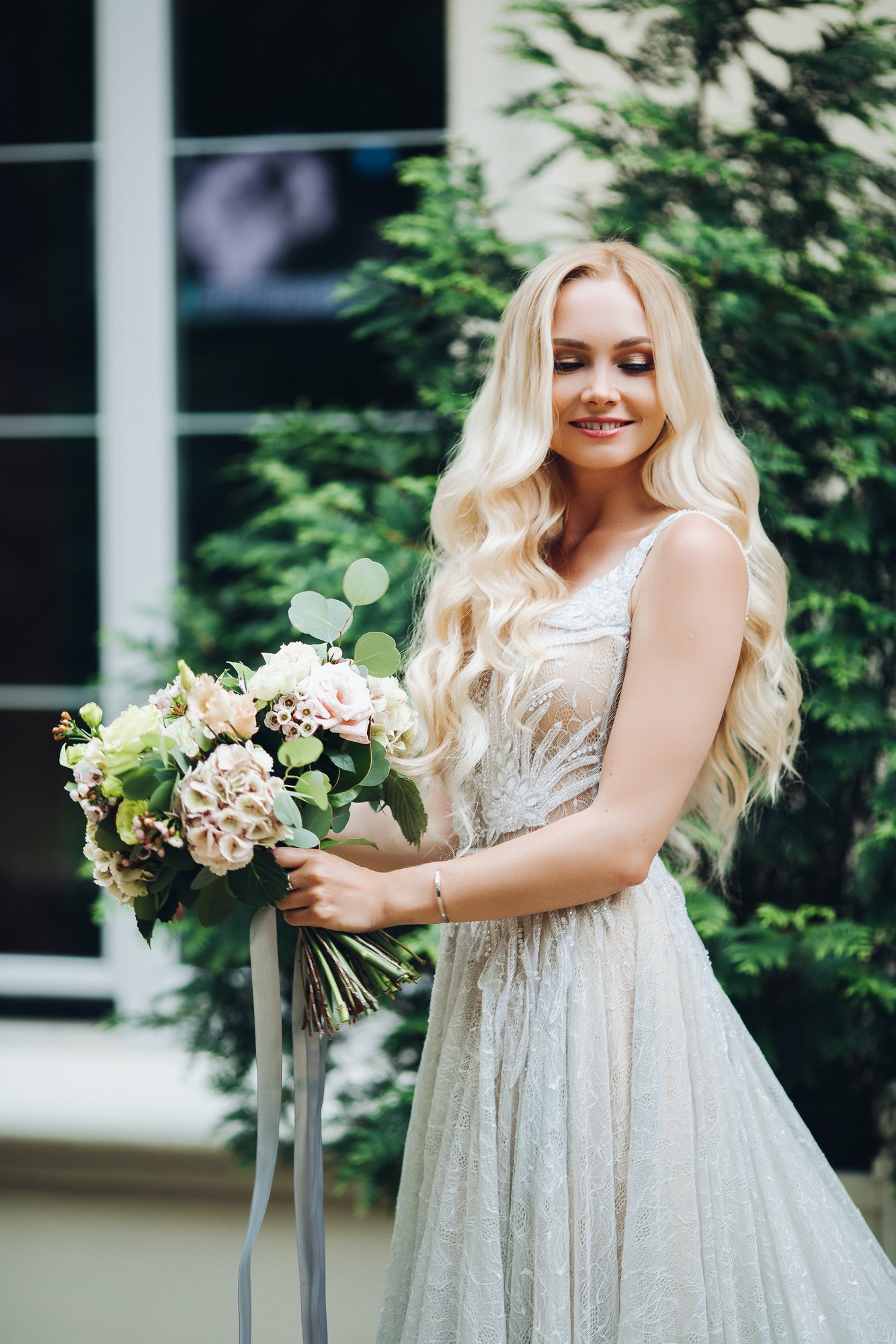 Elegant blondie bride smiling, holding wedding boquet.