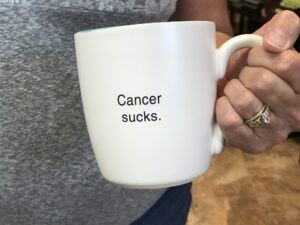 A woman holds a coffee cup that says cancer sucks